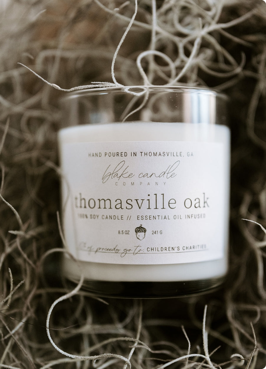 Thomasville Oak scented candle resting on pile of straw