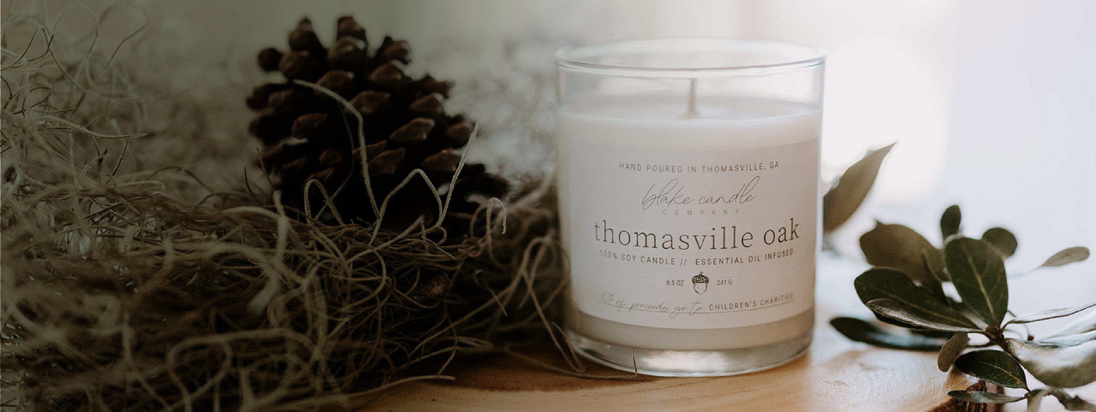 100% soy wax candle in thomasville oak scent on table top with greenery